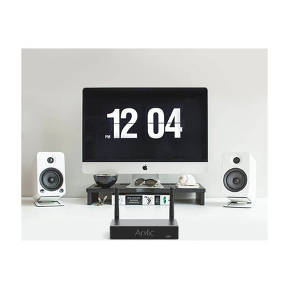 Computer monitor with digital clock display, flanked by two speakers on a white surface.